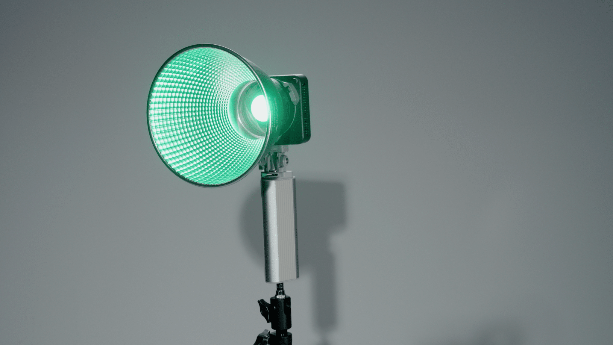 Green studio floodlight on an adjustable stand emitting a bright green glow in a neutral-gray studio setting.