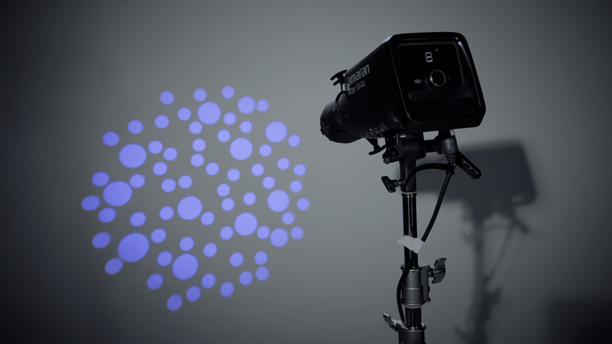 Studio strobe light on a stand projecting blue circular light orbs against a gray background, used for photography.