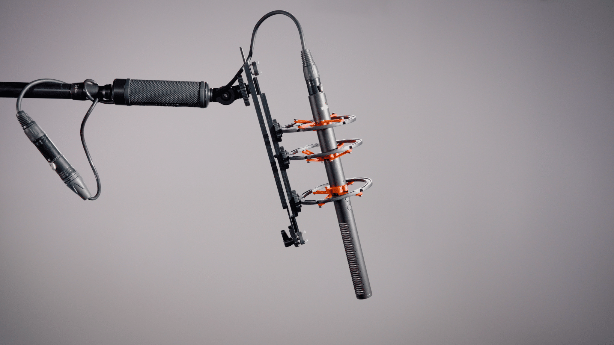 Professional studio microphone mounted in a shock cradle with XLR cable against a gray gradient backdrop, ready for recording.